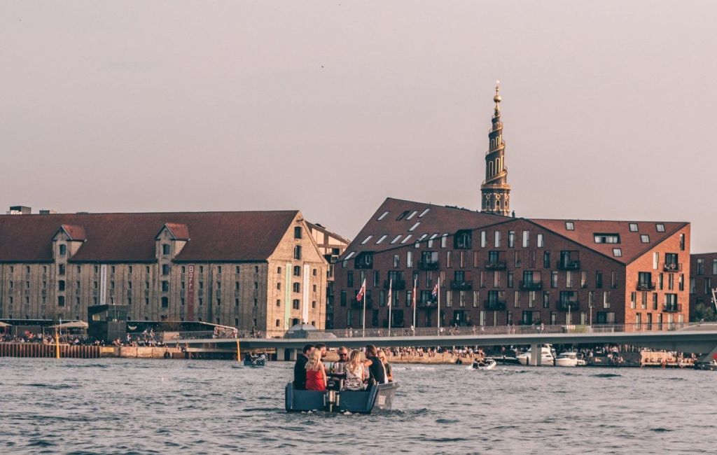 Barquinho pelas águas de Copenhague com torre da Igreja Nosso Salvador ao fundo 