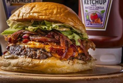 Hambúrguer do Mr. Mills criado para o evento com burger de 130g, queijo cheddar, cebola roxa assada e temperada, farofa de bacon, maionese Mills, ketchup Heinz Bacon e cebola caramelizada, alface americana picada no pão de brioche