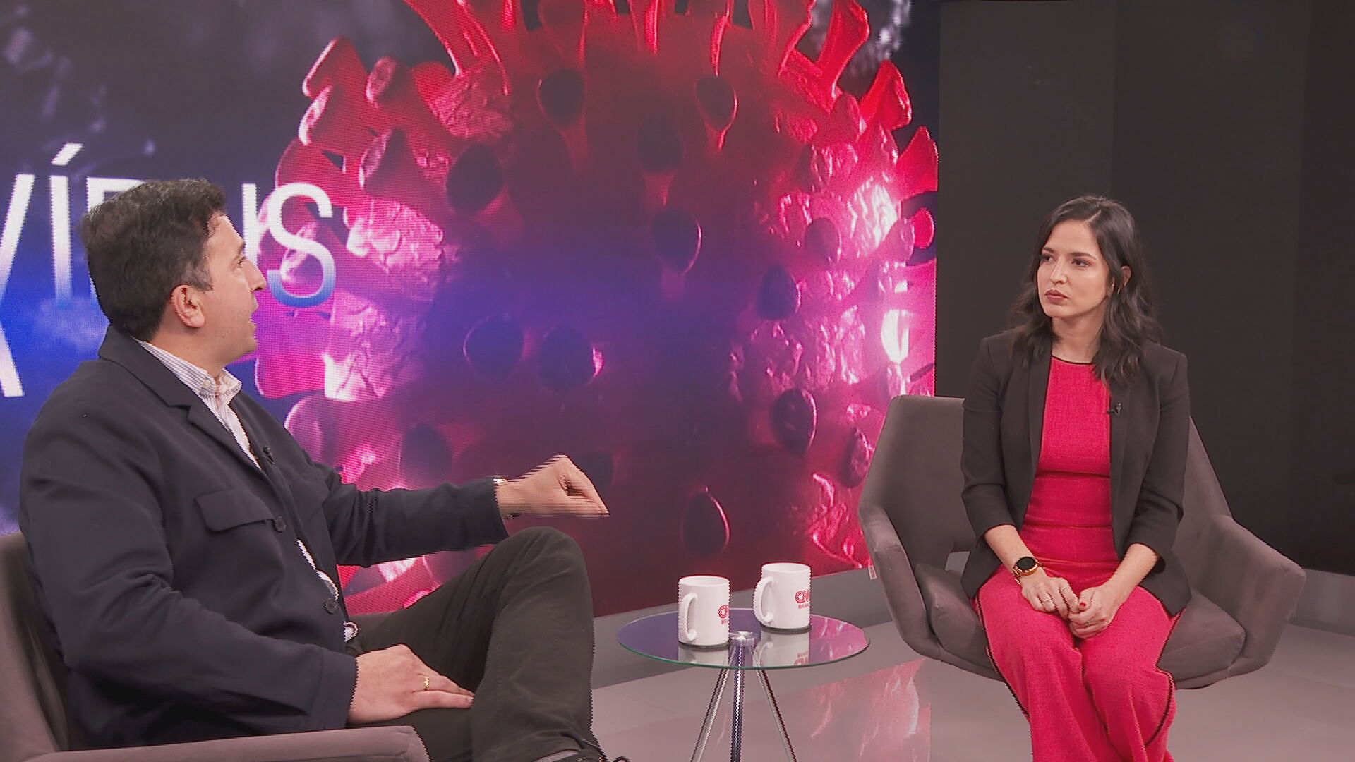 Dr. Gustavo Cabral e Karla Chaves conversam em frente à fundo com coronavírus