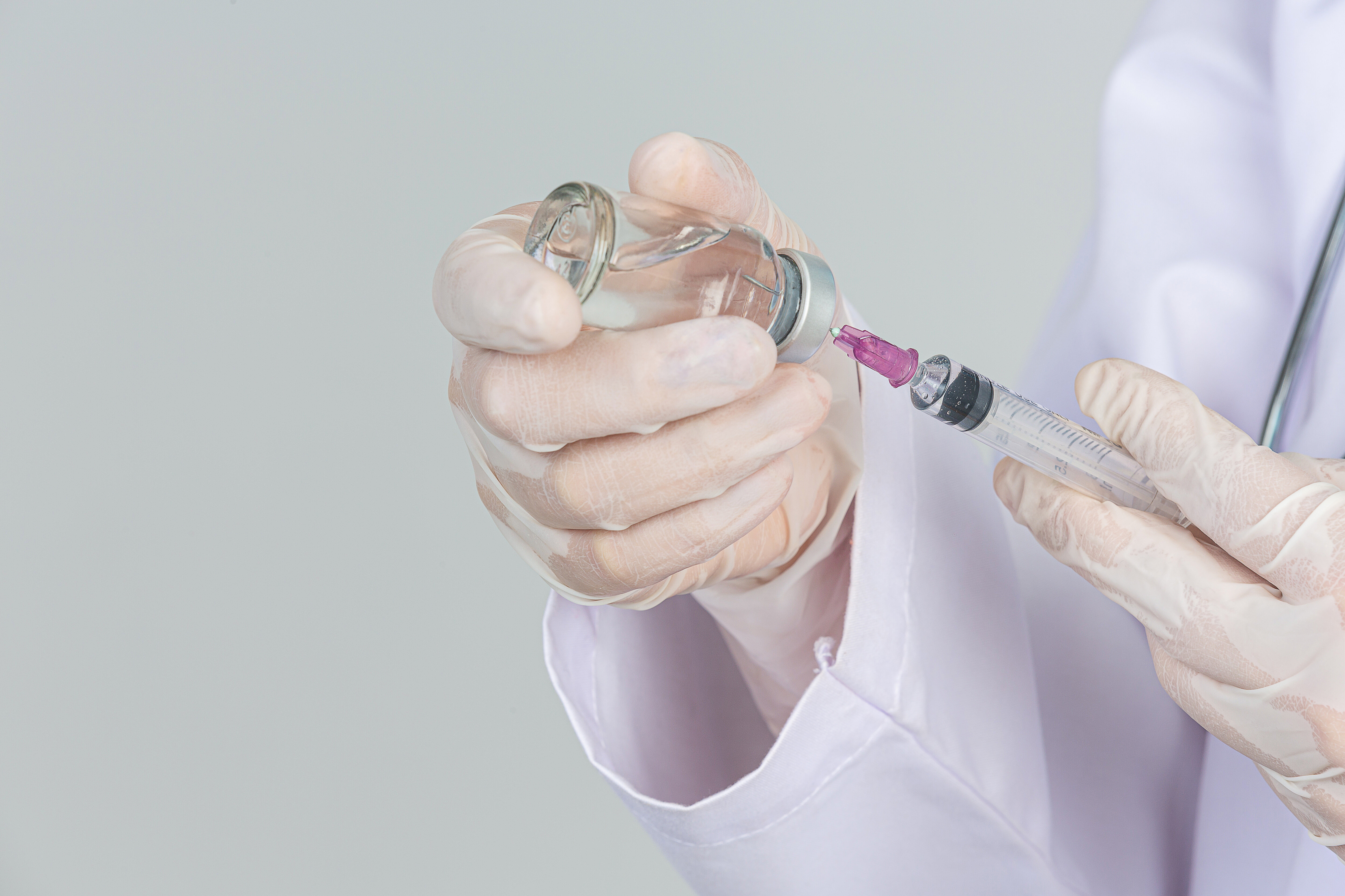 Médico de luvas colocando líquido em uma seringa