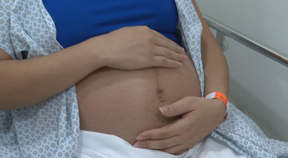 Com roupa de hospital, mulher na reta final da gravidez coloca a mão na barriga