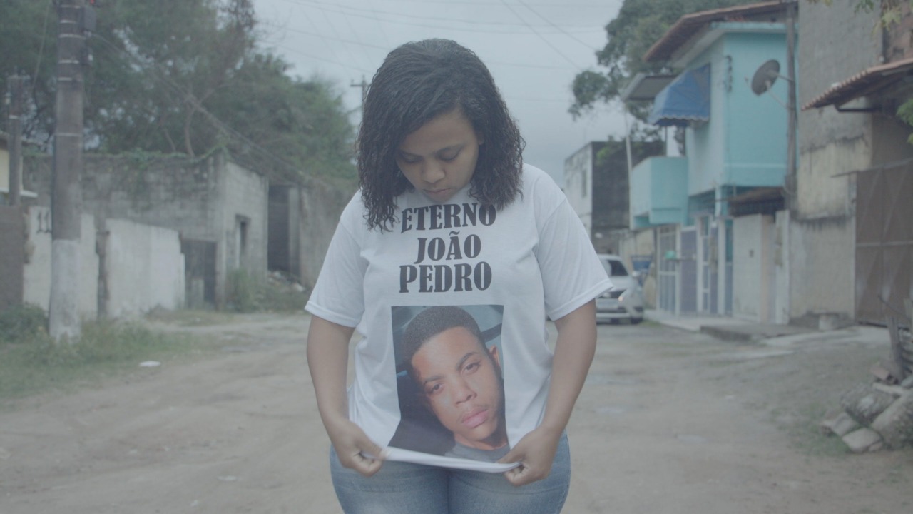 Mulher segura camiseta com a foto de João Pedro e os dizeres "Eterno João Pedro"