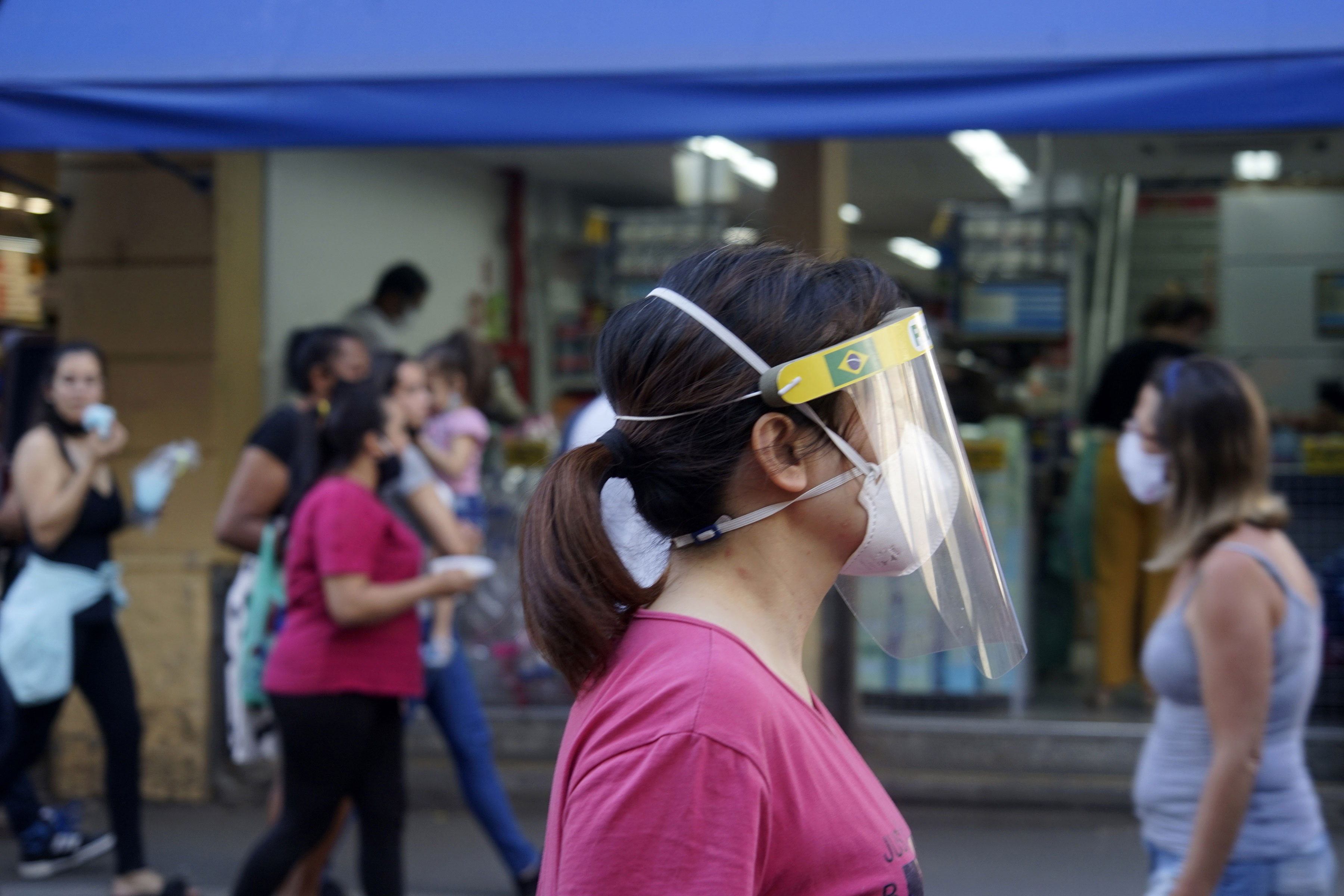Pedestre usa máscara e face shield ao andar pela 25 de março