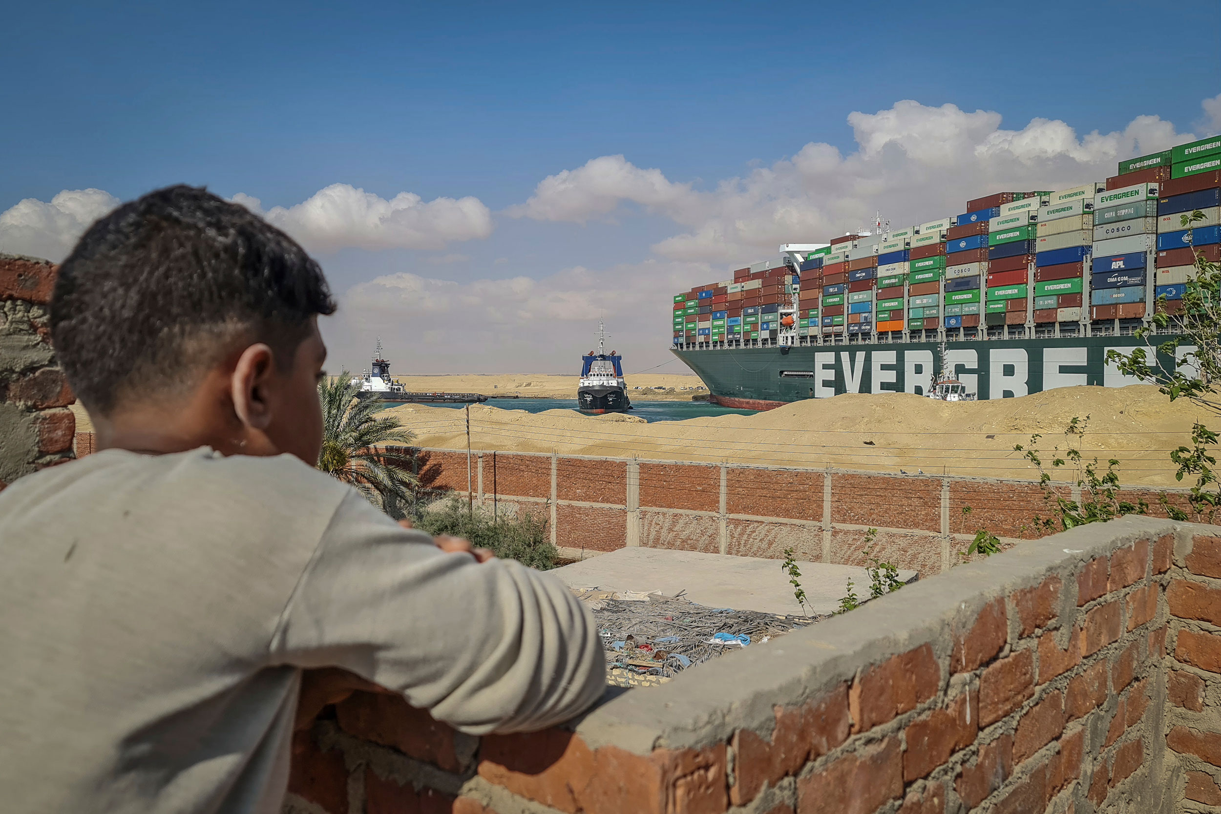 Garoto observa rebocadores tentarem desencalhar navio no canal de Suez