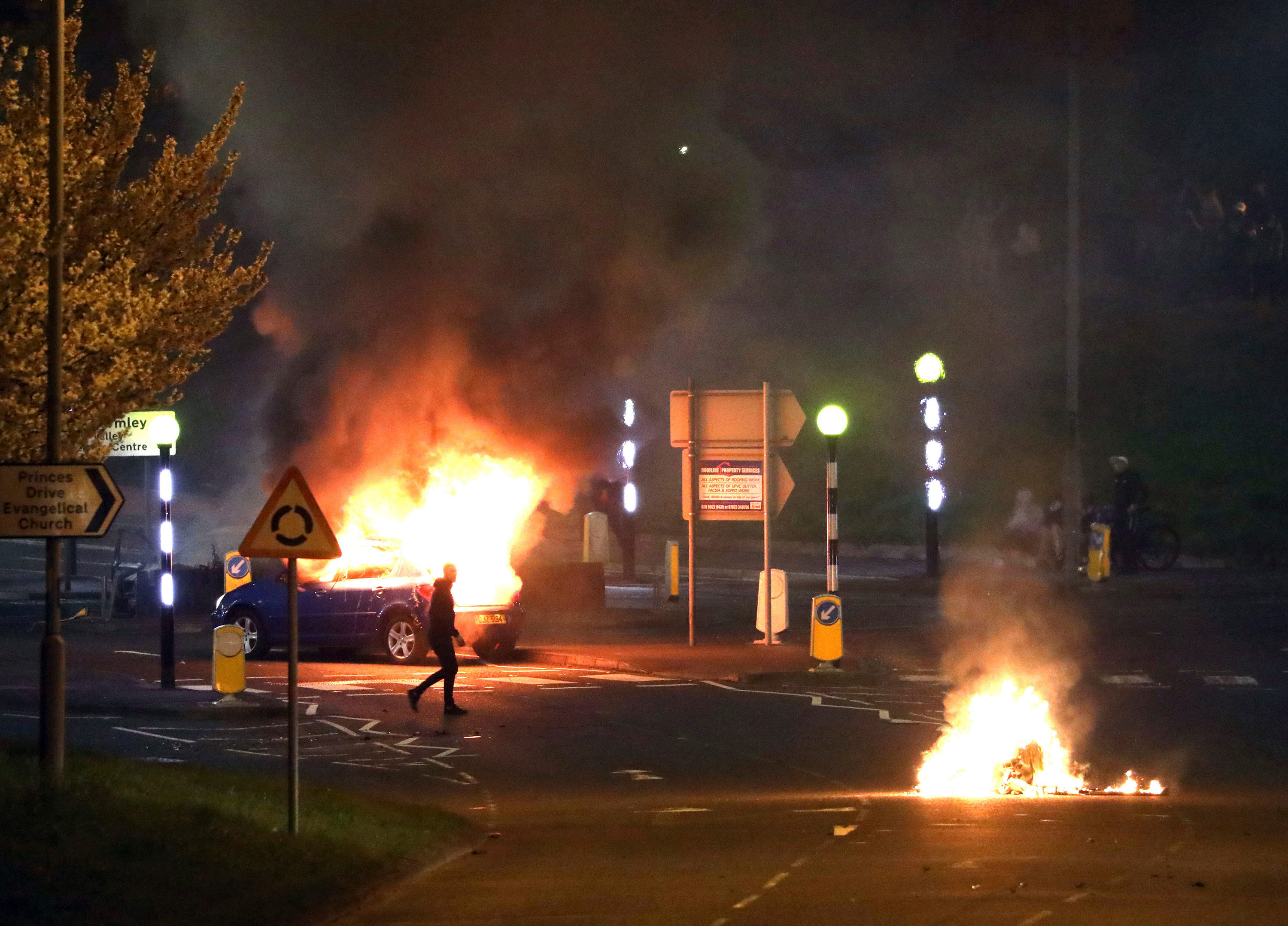 Homem caminha na frente de carro pegando fogo em Belfast, no norte da Irlanda