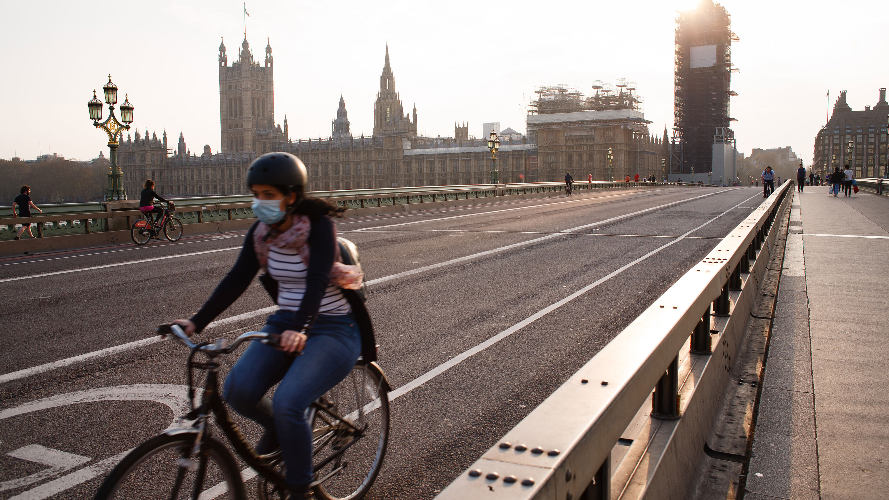 Mulher usa máscara enquanto pedala em frente ao Parlamento inglês, em Londres