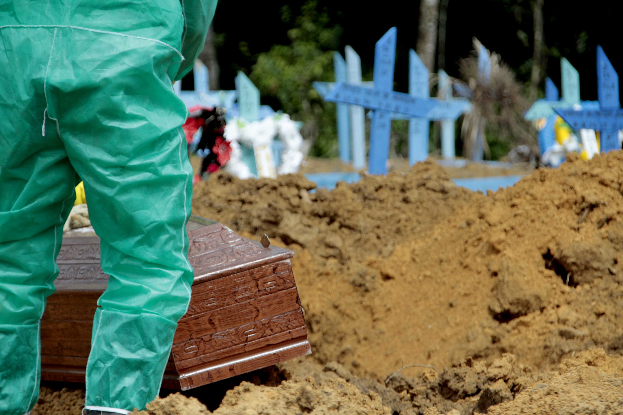 Coveiro em traje de proteção sepulta caixão em cemitério de Manaus