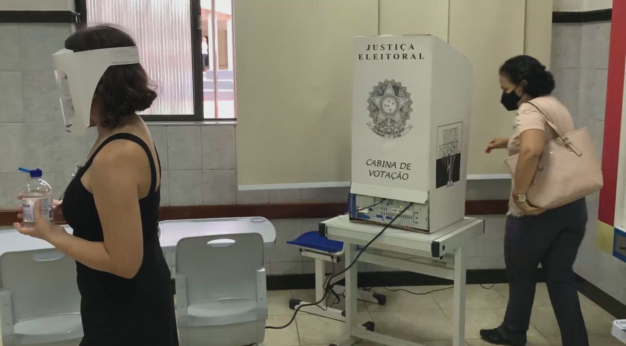 Eleitora e mesária cumprem as protocolos de segurança em local de votação