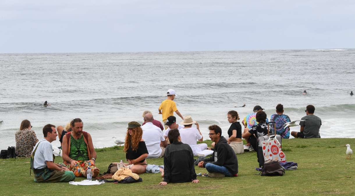 Pessoas sentam na grama ao lado da praia em Byron Bay, na Austrália