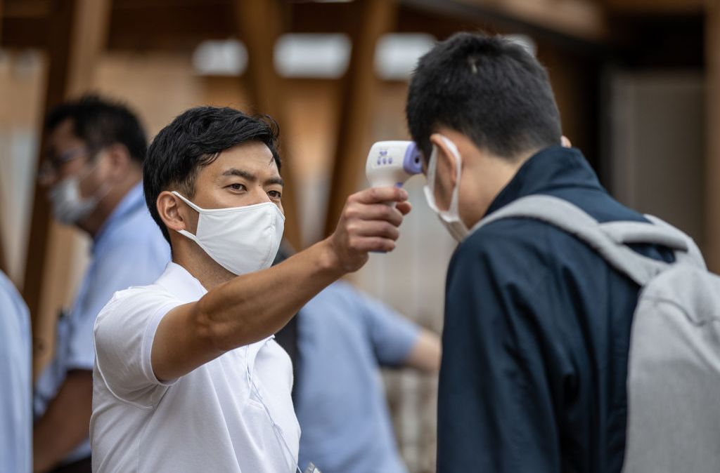 Funcionário checa a temperatura de homem durante apresentação à imprensa do Village Plaza, parte da vila ollímpica de Tóquio - 20.jun.2021