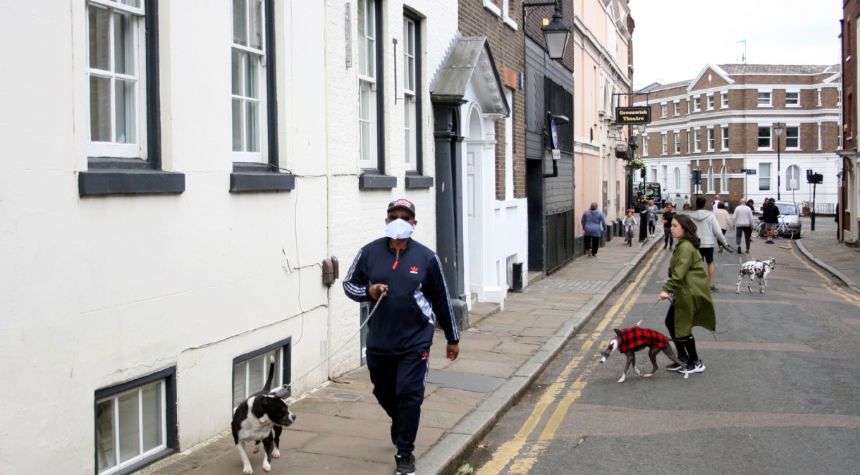 Homem com máscara caminha com cachorro em Greenwich, Londres