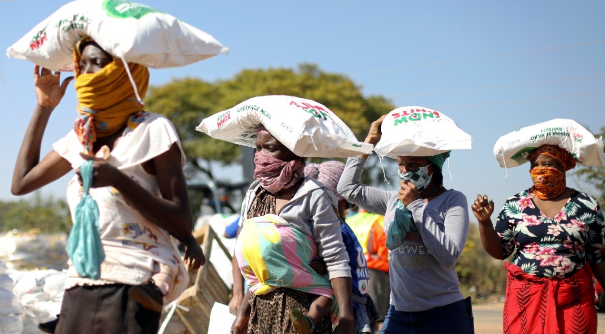 Mulheres carregam saco de milho recebido de doação em Pretória, na África do Sul 