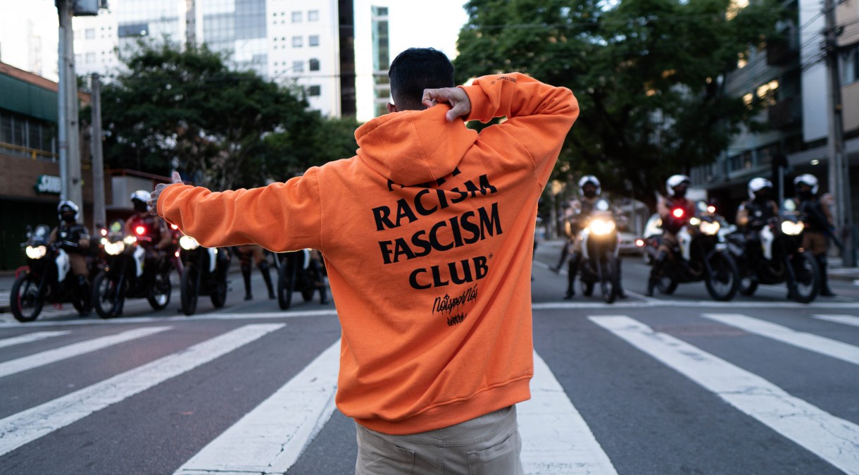 Manifestante usando casaco com as palavras "Anti Racism Fascism Club" se posiciona em frente a policiais durante manifestação em Curitiba (7.jun.2020)