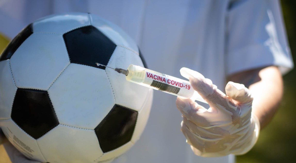 Bola de futebol ao lado de seringa e ampola em alusão à vacina para Covid-19