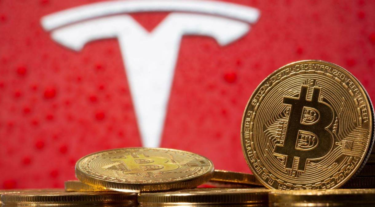 Representação da moeda virtual bitcoin, com logotipo da Tesla ao fundo.