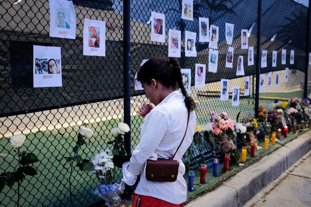 Flórida: Mulher reza em frente a mural de fotos de desaparecidos em desabamento