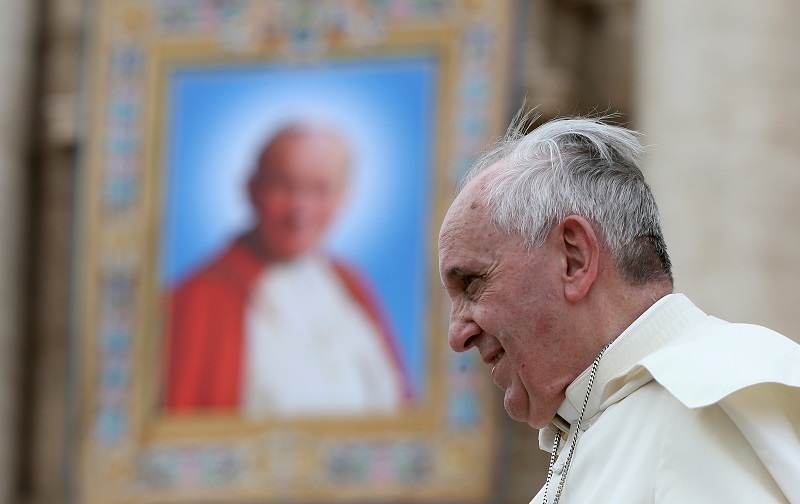 Papa Francisco passa ao lado de uma tapeçaria do falecido Papa João Paulo II