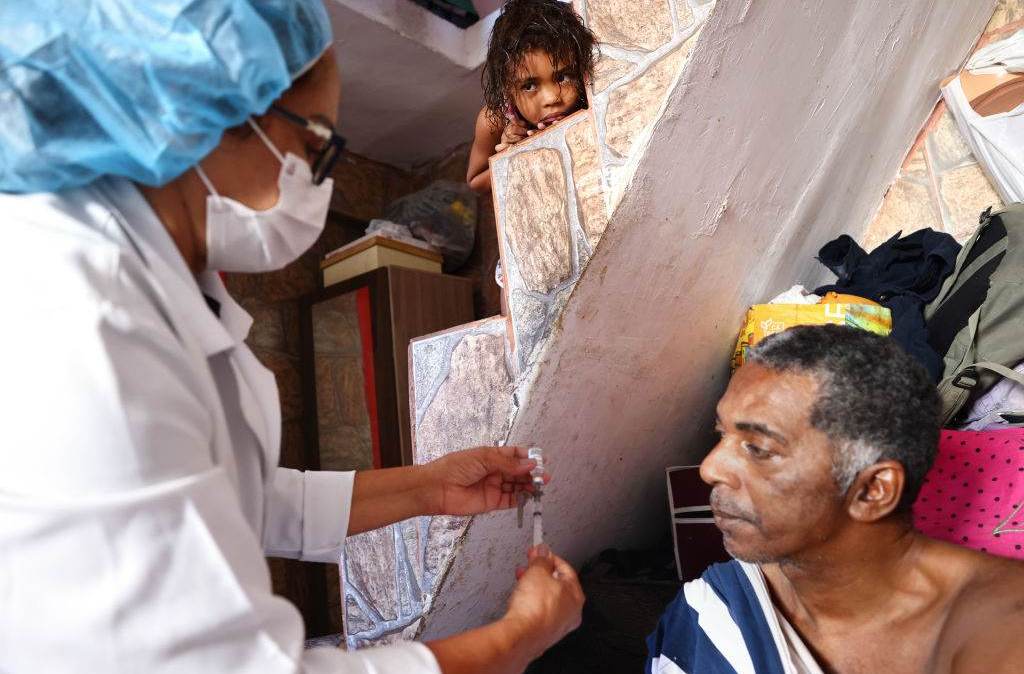 Enfermeira do SUS aplica vacina contra Covid-19 em homem em sua casa na Rocinha, no Rio, em uma das rondas frequentes que profissionais de saúde fazem na comunidade para imunizar pessoas que não querem ir ao posto