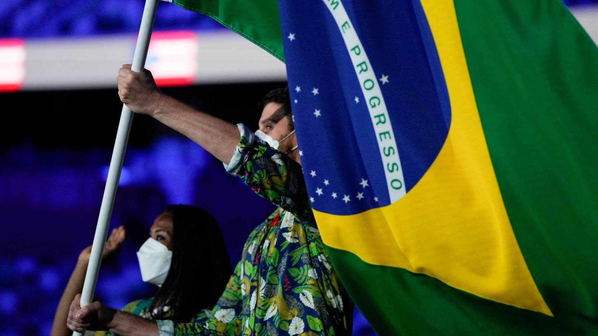 Acompanhado de Ketleyn Quadros, Bruninho, do vôlei, carrega a bandeira do Brasil