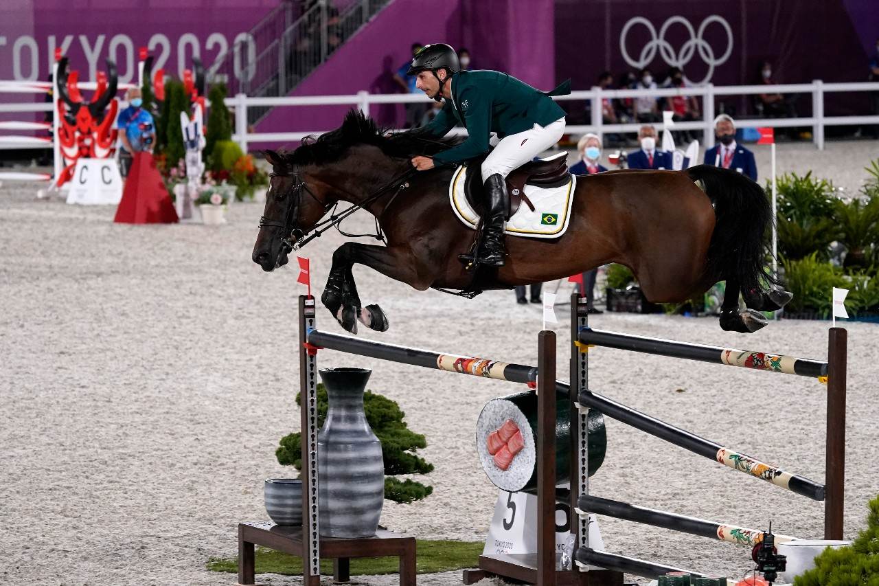 Atleta do hipismo, vestindo roupa verde, salta obstáculo com o cavalo