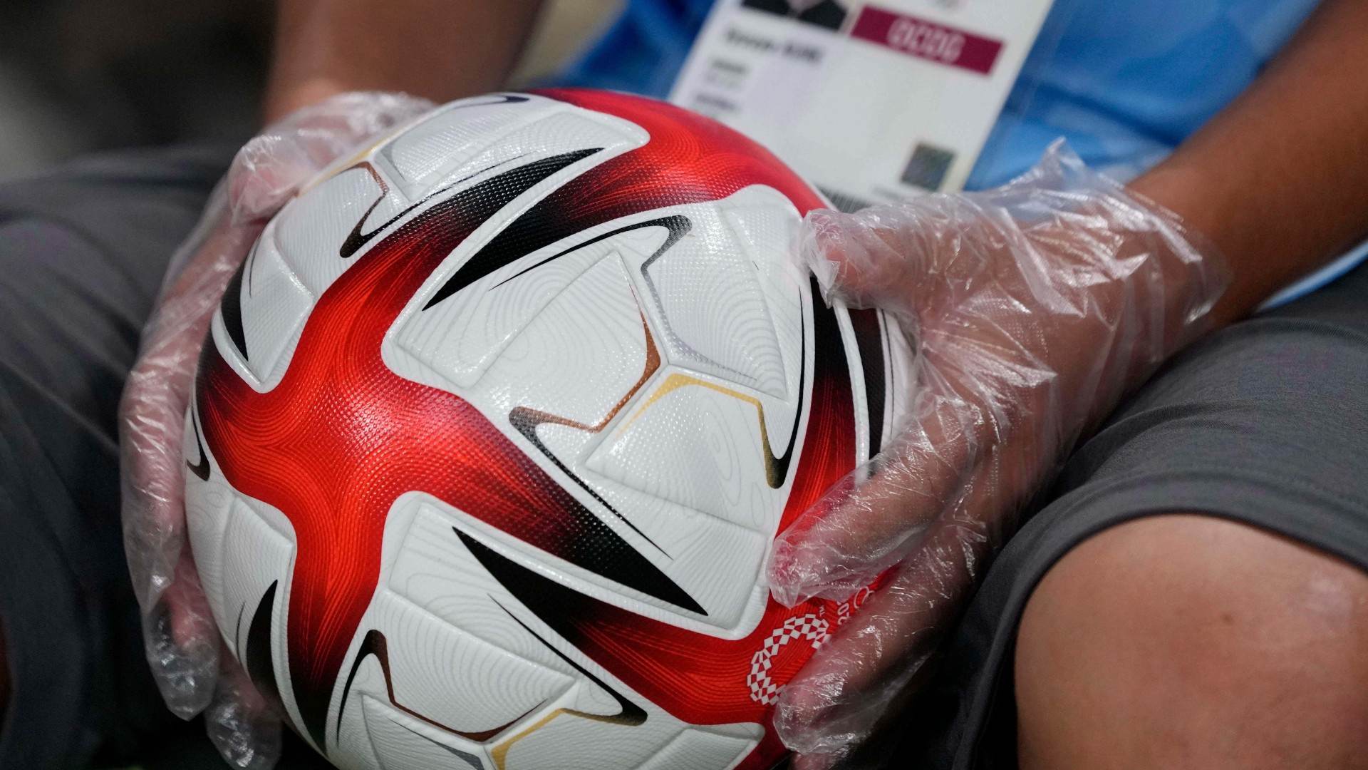 Voluntário em Tóquio usa luvas para segurar bola de futebol nos Jogos