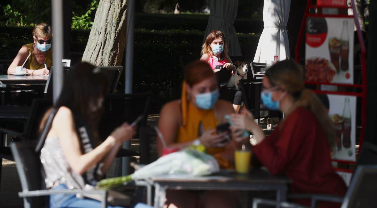 Pessoas com máscara de proteção sentam em mesas de quiosque no Parque del Retiro, em Madrid