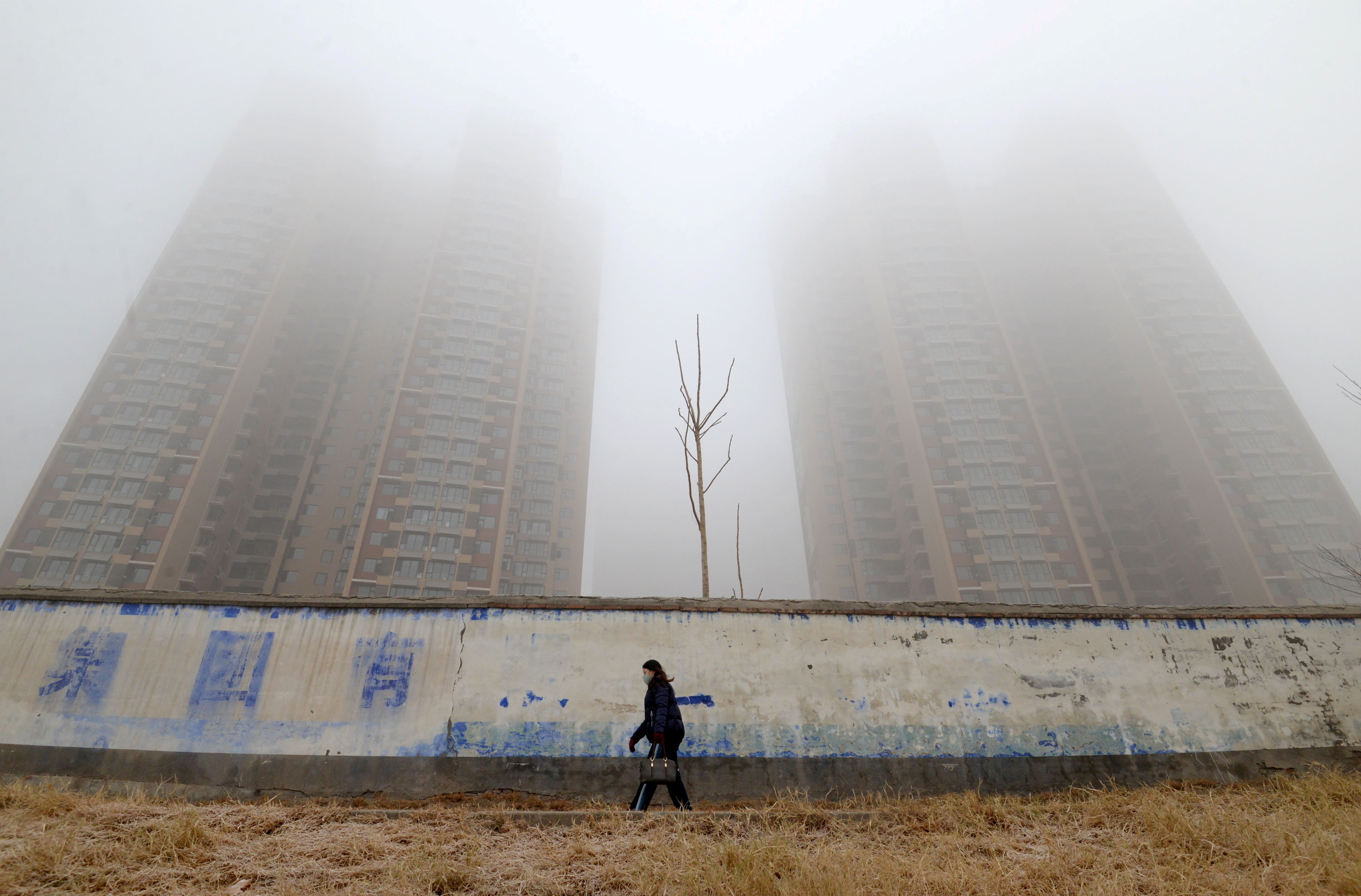 Mulher usando máscara caminha perto de prédios em meio à poluição em Hebei, na China