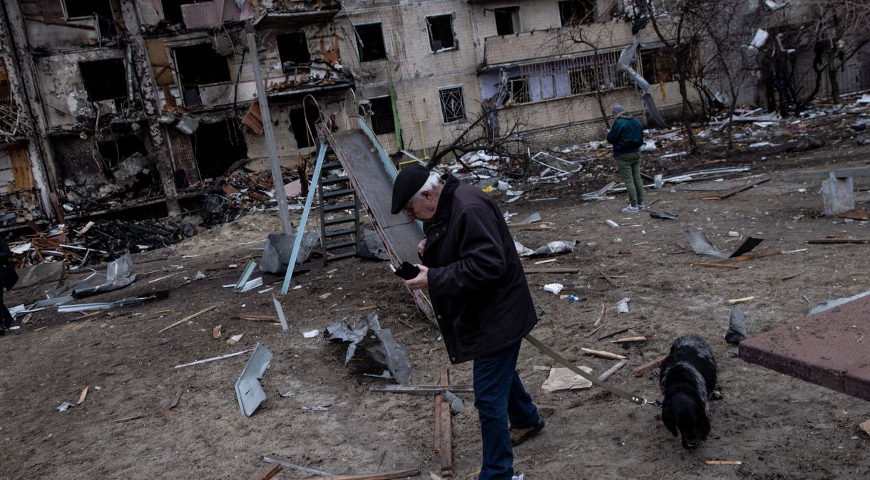 Um homem caminha com seu cachorro na frente de um bloco residencial danificado por um ataque de mísseis matinal, em 25 de fevereiro de 2022, em Kiev.
