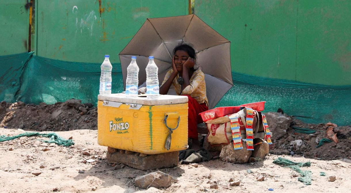 Uma garota vende água e usa um guarda-chuva para se proteger do sol enquanto espera clientes em Nova Délhi, Índia, em 27 de abril.