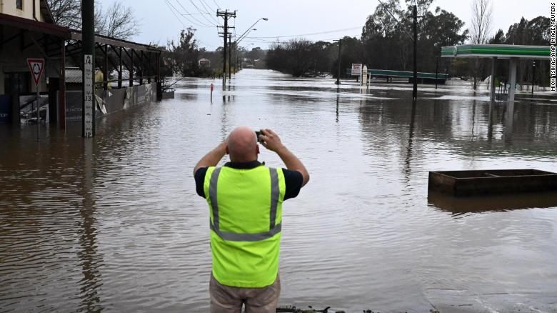 Um local tira uma foto de uma estrada inundada por enchentes em Camden, no sudoeste de Sydney, domingo, 3 de julho de 2022.