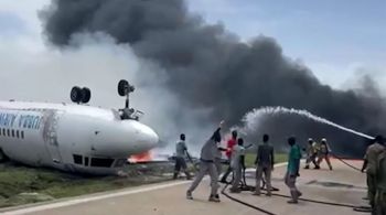 Fumaça preta e chamas subiram em direção ao ar enquanto caminhões de bombeiros se aproximaram da pista e os bombeiros começaram a disparar água contra o avião acidentado