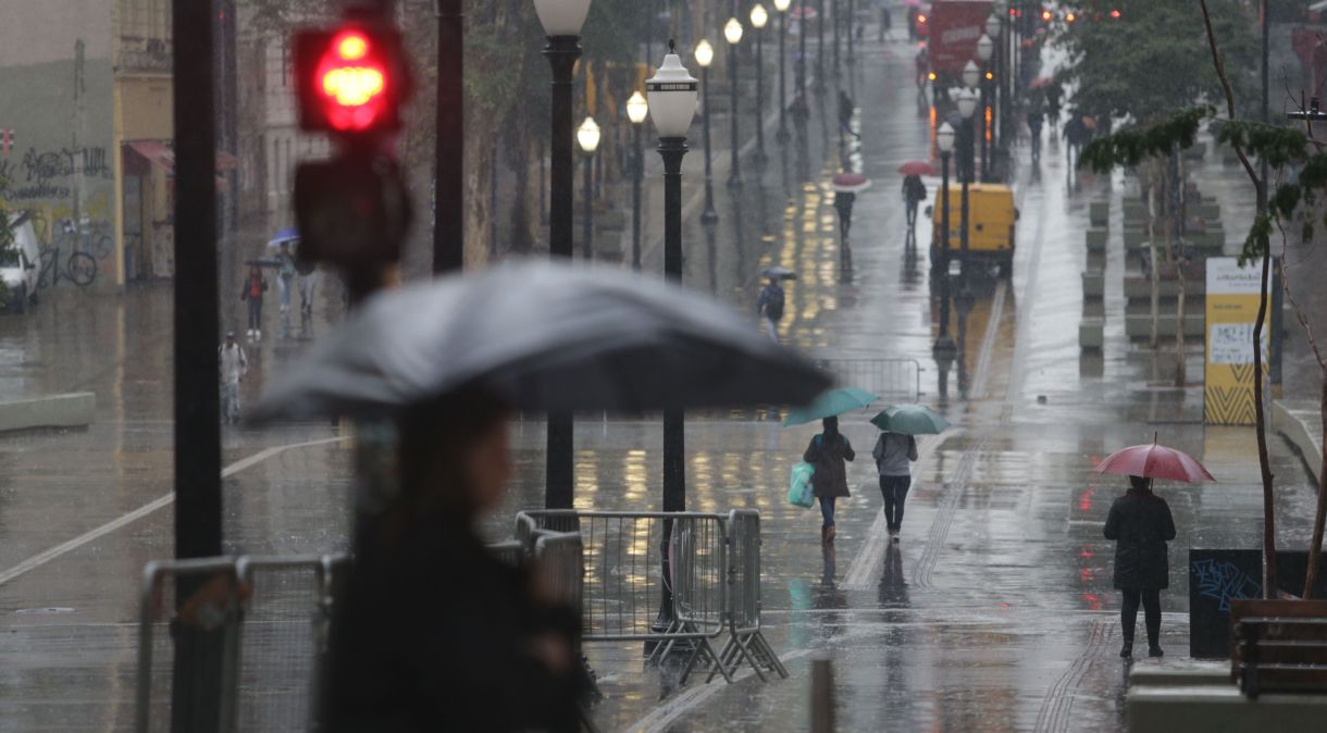 Pedestres se protegem do frio e da chuva no centro da cidade de São Paulo.