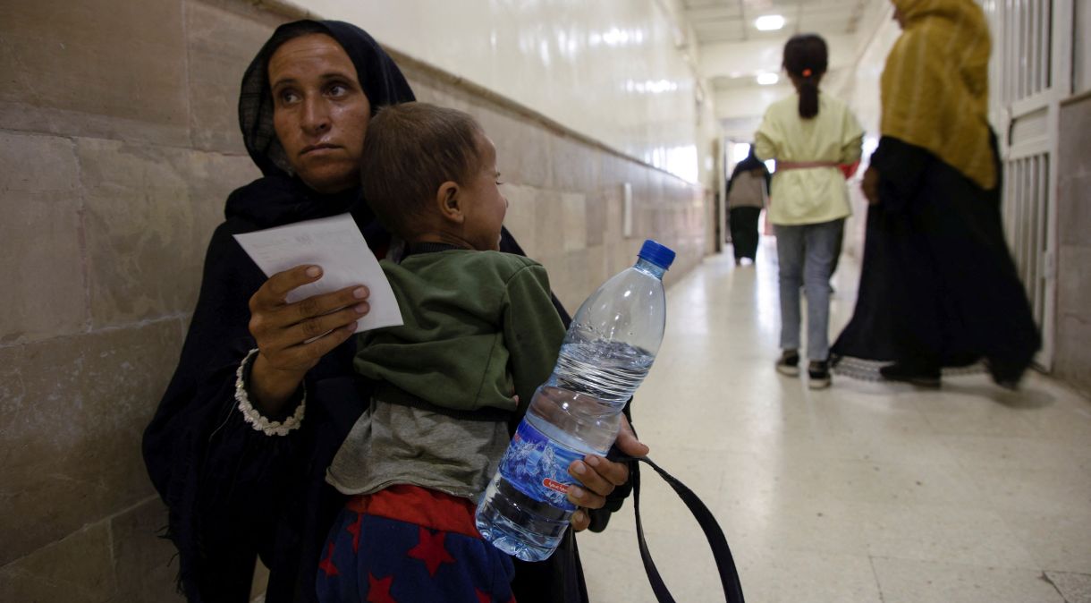 Mulher carrega filho com suspeita de cólera em Hasaka, na Síria