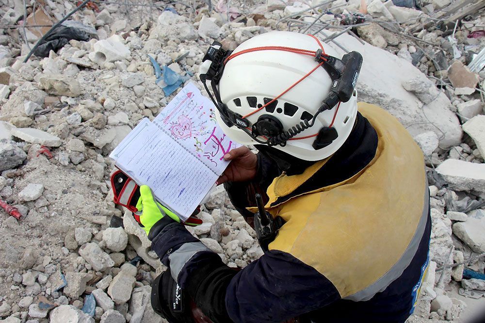 Um membro dos Capacetes Brancos examina um caderno encontrado nos escombros