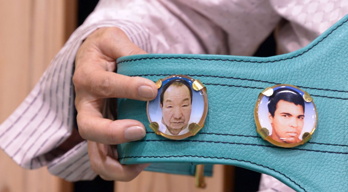 O rosto do ex-boxeador Iwao Hakamada estampado em um cinturão ao lado da imagem de Muhammad Ali.