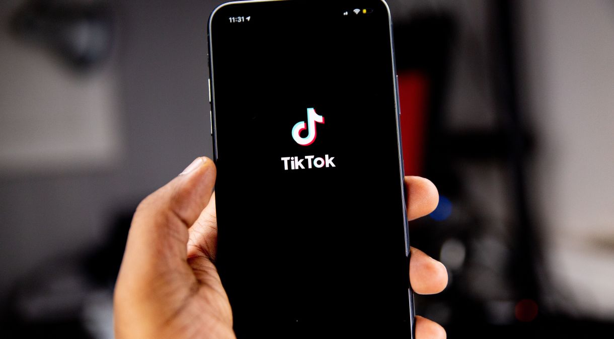 Pessoas segurando celular, que exibe na tela o aplicativo TikTok