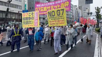 Fortemente cercados por policiais, pessoas protestam carregando placas dizendo “não ao G7 imperialista” e “tirem as mãos da Ucrânia”