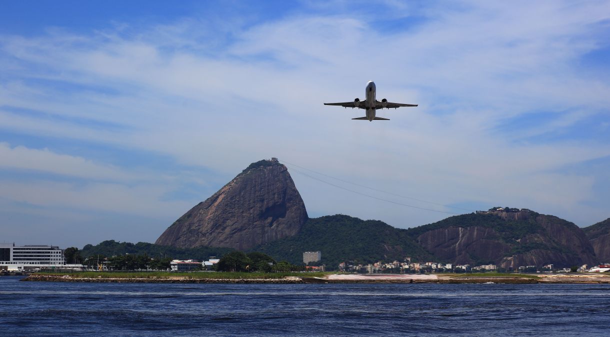 Avião pousando no aeroporto Aeroporto Santos Dumont, no Rio de Janeiro; ao fundo o Pão de Açúcar