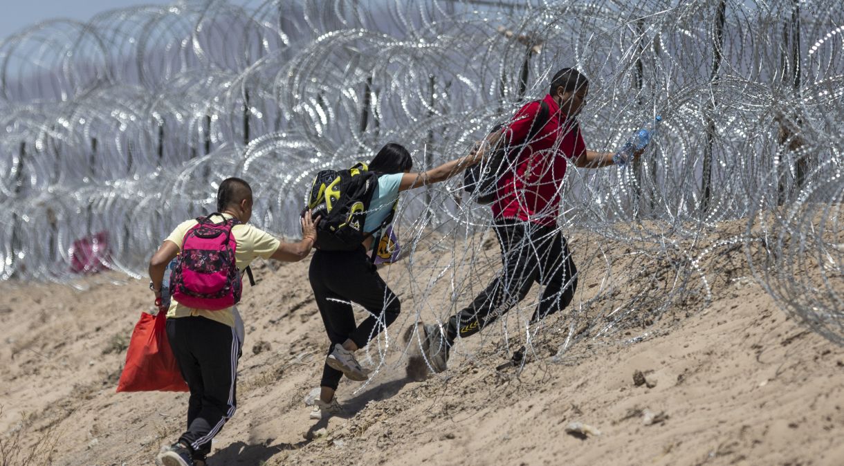 Imigrantes atravessam arame farpado em torno de um acampamento improvisado depois de cruzar a fronteira do México, em 11 de maio de 2023 em El Paso, Texas