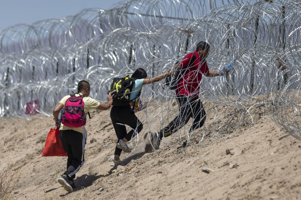 Imigrantes atravessam arame farpado em torno de um acampamento improvisado depois de cruzar a fronteira do México, em 11 de maio de 2023 em El Paso, Texas