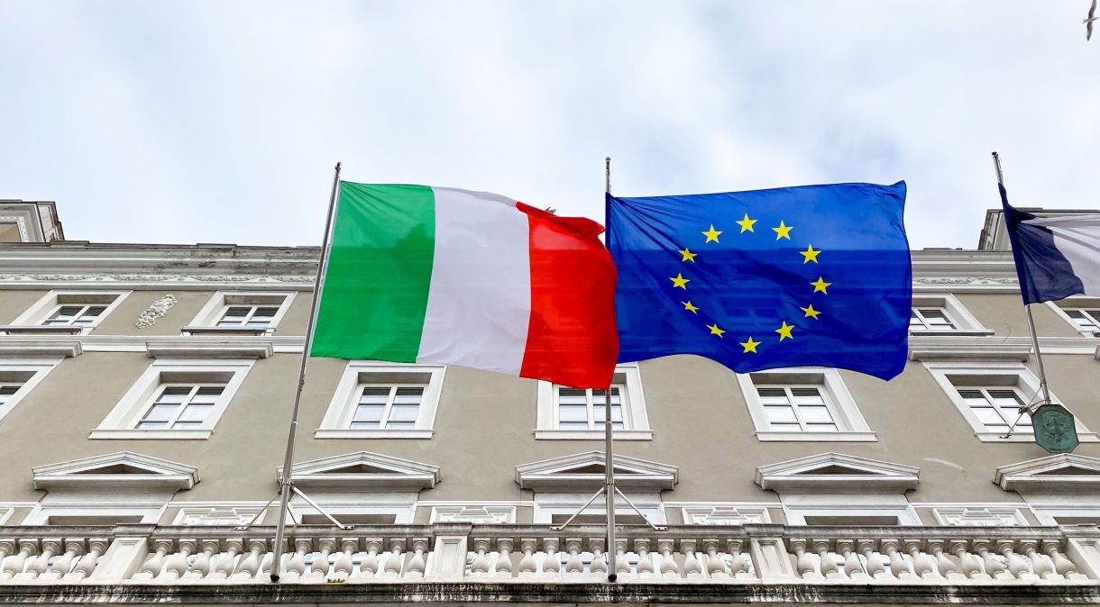 Bandeira da Itália e bandeira da União Europeia hasteadas em frente a um prédio