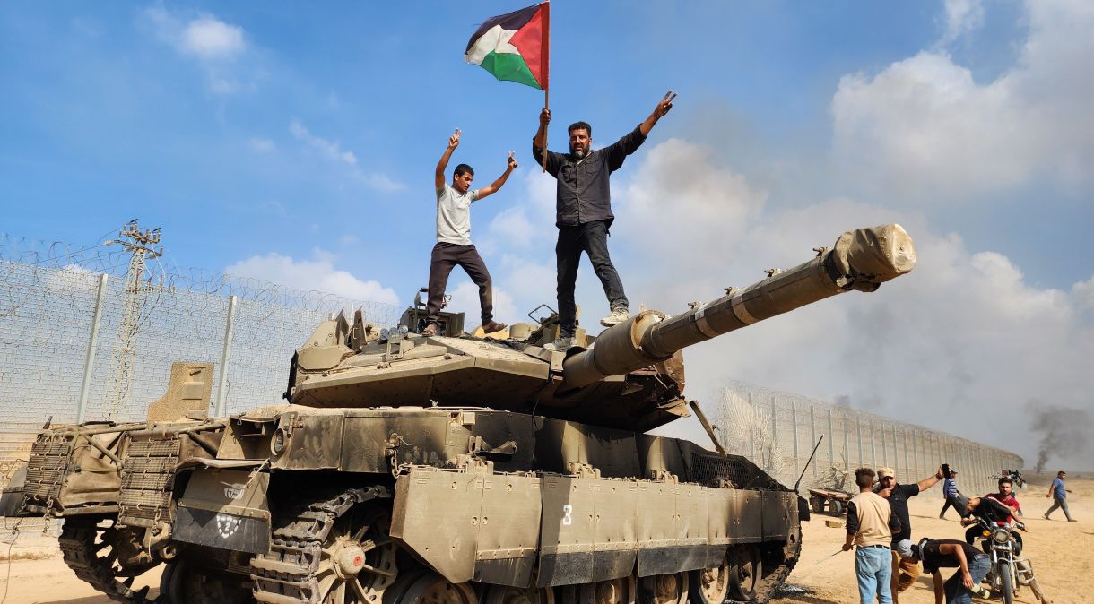 As Brigadas Izz ad-Din al-Qassam seguram uma bandeira palestina enquanto destroem um tanque das forças israelenses na cidade de Gaza