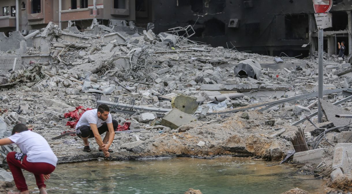 Homem palestino lava as mãos em uma poça ao lado de um prédio destruído após os ataques israelenses na Cidade de Gaza