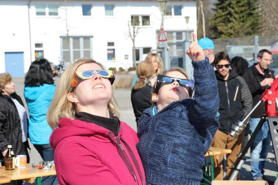 Mulher com criança no colo observam o sol com óculos especiais de proteção solar