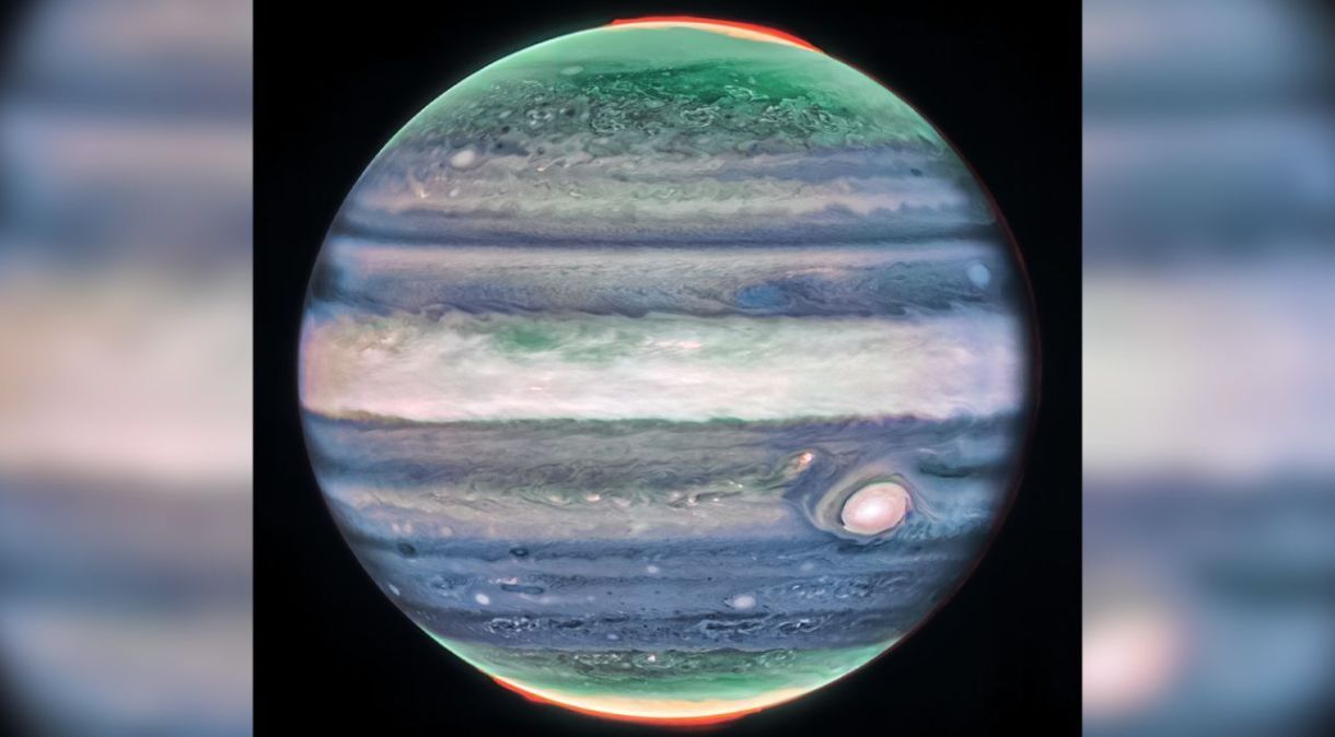 A câmera infravermelha próxima do Telescópio Espacial James Webb capturou uma imagem de Júpiter em luz infravermelha. As manchas e listras brancas brilhantes são provavelmente topos de nuvens de tempestades em alta altitude. Auroras, mostradas em vermelho, podem ser vistas ao redor dos polos