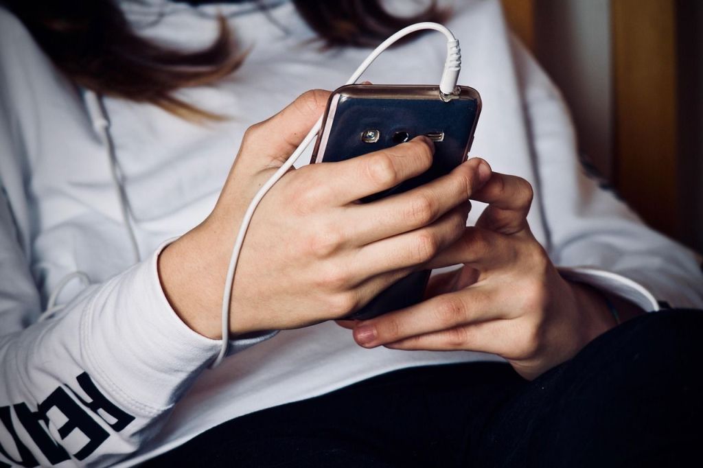 mão de uma adolescente segurando um celular com fone plugado