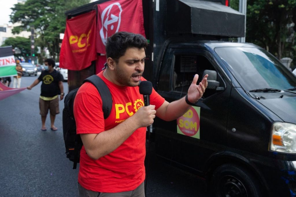 Foto mostra João Pimenta com uma camisa vermelha discursando na rua próximo a um caminhão