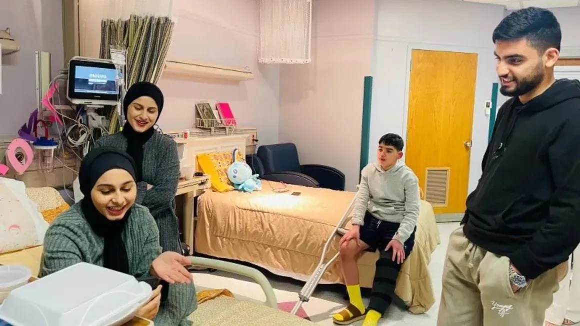 Ayham Musalm, de 13 anos, no centro, está recebendo tratamento para uma perna fraturada e estilhaços de vidro alojados em seu joelho. Ele ficou ferido quando os destroços de um ataque à casa de um vizinho atingiram sua casa