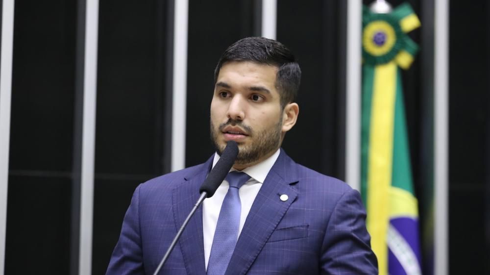 A foto mostra o deputado federal André Fernandes no Plenário da Câmara. Ele veste terno azul, gravata azul clara e tem cabelo preto.