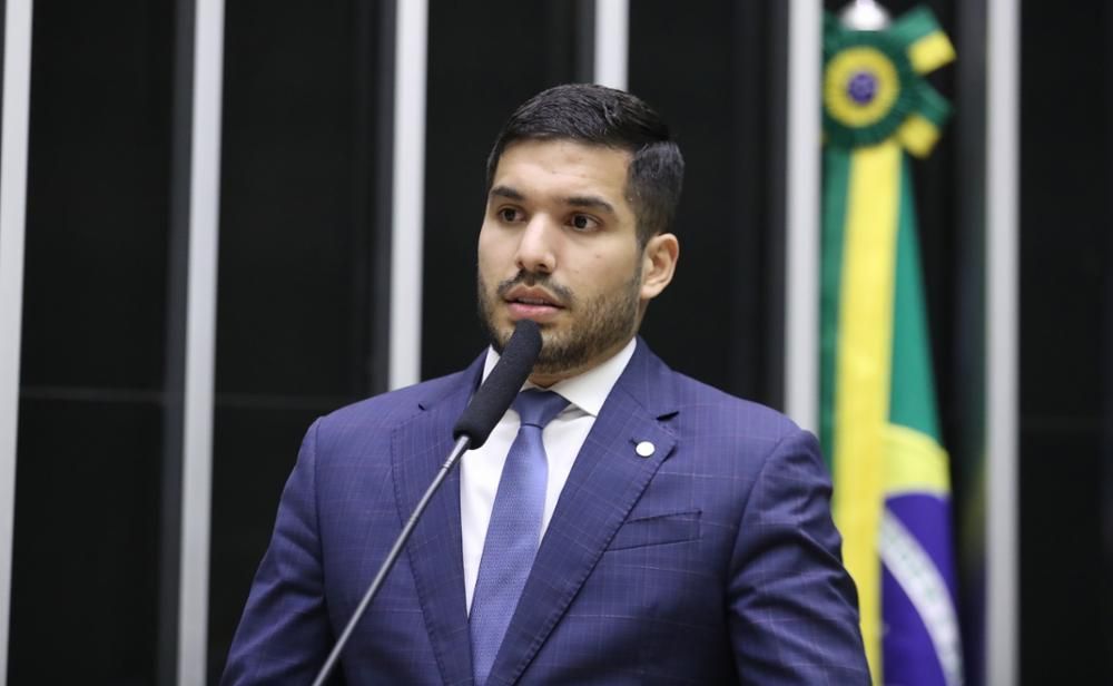 A foto mostra o deputado federal André Fernandes no Plenário da Câmara. Ele veste terno azul, gravata azul clara e tem cabelo preto. 
